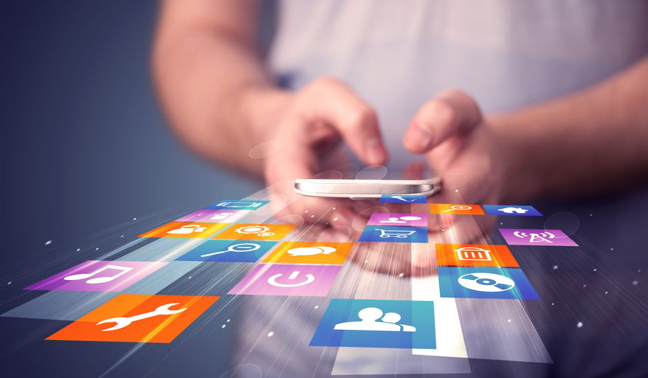 A person holding a smartphone with colorful app icons floating around it, including a wrench, music note, and shopping cart—showcasing a vibrant display of mobile app strategy. The blurred background emphasizes the importance of effective app development ROI.