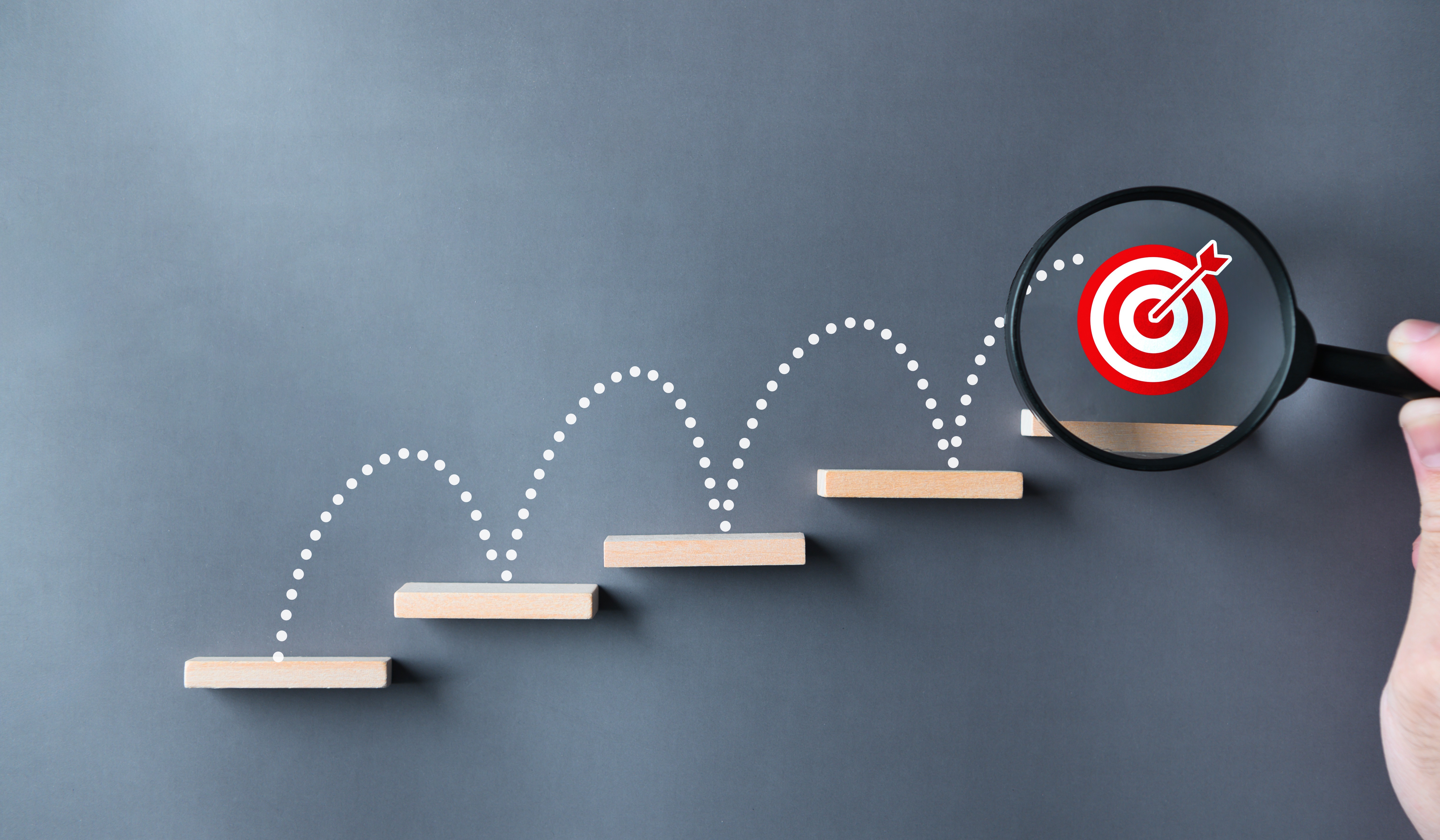 Magnifying glass focusing on target at top of ascending steps, representing the progression from AI pilots to scaled enterprise results